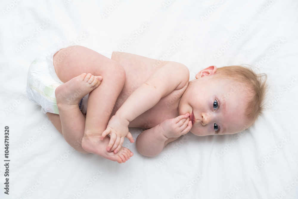 healthy baby sucks his hand and lies on back on white bed linen. healthy baby sucks his hand and lies on back on white bed linen.