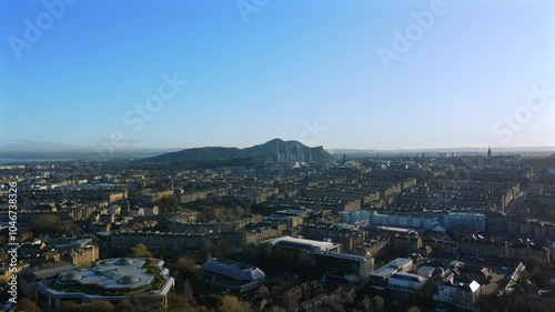 Drone footage of Edinburgh, Scotland, showcasing a panoramic cityscape with Arthur’s Seat in the background. The shot captures historic buildings, modern structures, and streets.