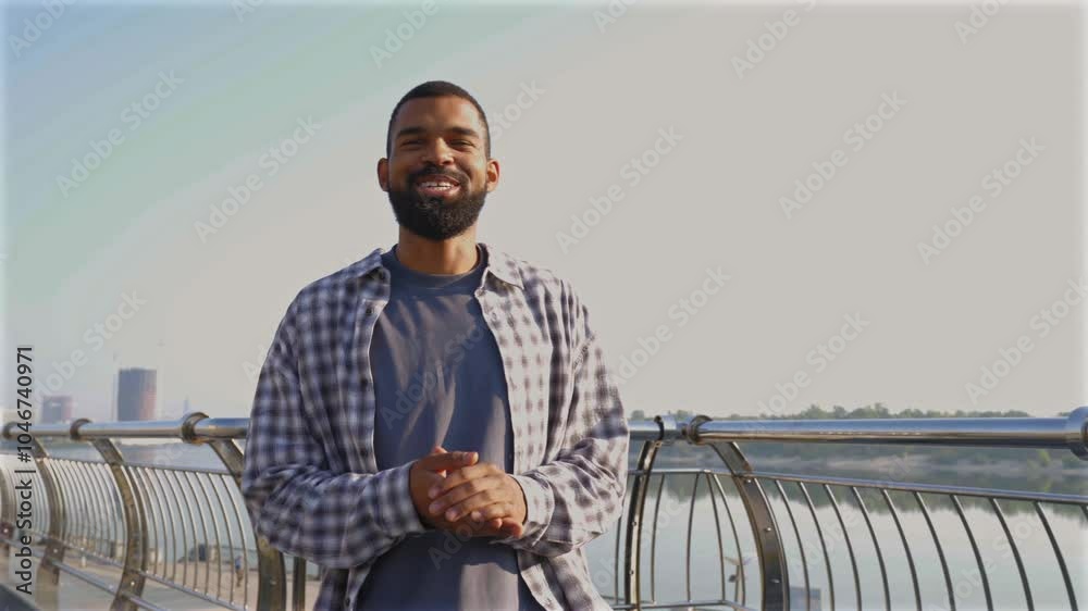 Positive attractive cool bearded African American man blogger live streaming vlog, communicating and sharing with online audience while walking on city street on sunny summer day