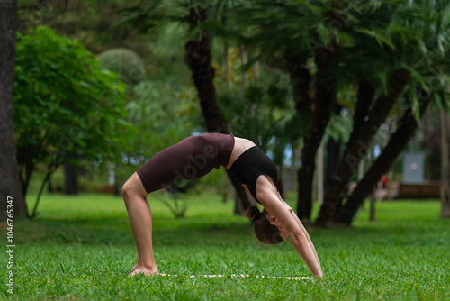 Young woman in sportswear performing urdhva dhanurasana, also known as bow up pose, bridge or wheel pose, on mat in park. Beautiful athletic flexible girl in the park on the mat photo