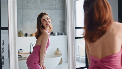 Joyful woman trying dress admiring stylish look in bathroom mirror closeup.