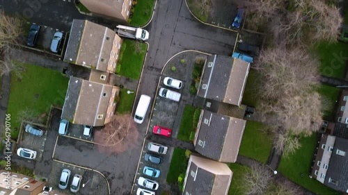 Top-Down view of a residential area in Edinburgh, featuring buildings, parking lots, and roadways. Cars are visible on streets and driveways, with green spaces and trees between housing units.