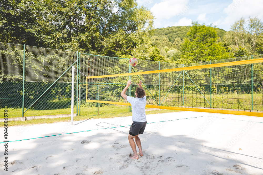 Volleyball player setting the ball on a sand court, preparing for the next play during an outdoor beach volleyball game. The action highlights control and precision in the game Volleyball player setting the ball on a sand court, preparing for the next play during an outdoor beach volleyball game. The action highlights control and precision in the game