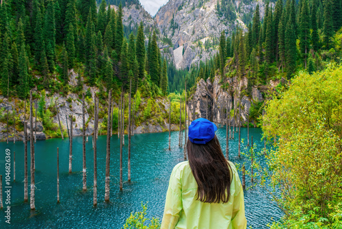 Young woman standing against a picturesque mountain landscape. Lake Kaindy is in the Kungey Alatau mountain range and is part of the northern Tien Shan. Kazakhstan, Kolsay Lakes National Park photo