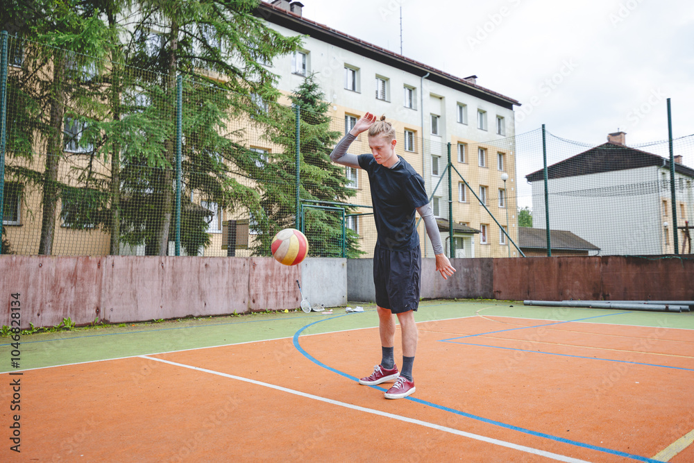 Fototapeta premium Volleyball player standing on a hard court, bouncing the ball while preparing for the next play during an outdoor game. A calm, focused moment before the action begins
