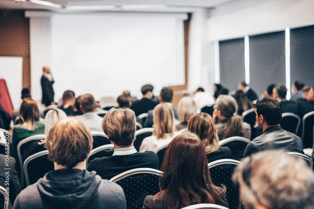 Speaker giving a talk in conference hall at business event. Rear view of unrecognizable people in audience at the conference hall. Business and entrepreneurship concept Speaker giving a talk in conference hall at business event. Rear view of unrecognizable people in audience at the conference hall. Business and entrepreneurship concept