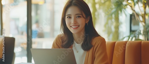 Asian woman smiling while typing on laptop in a modern office, natural light, professional setting, vibrant colors