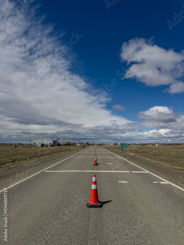 An empty road with an orange cone and a blue sky with clouds in the background.