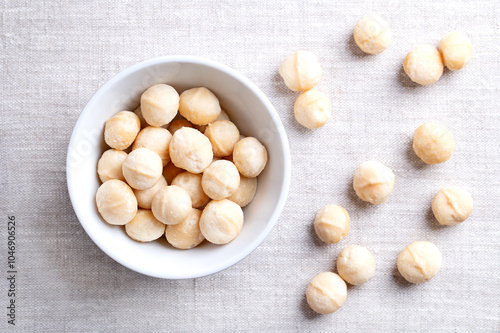 Macadamia nuts, roasted and salted, in a white bowl on linen fabric. Also known as Queensland nut, bush nut, maroochi nut, bauple and Hawaii nuts. Ready-to-eat snack nuts. Close-up, from above. Photo photo