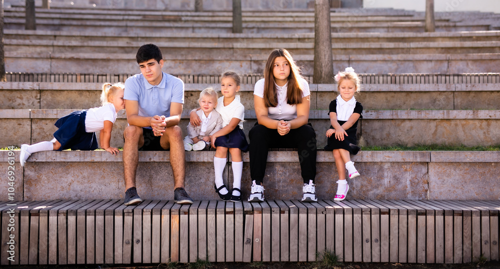 Obraz premium Children of different ages in school uniforms sitting on the steps outside