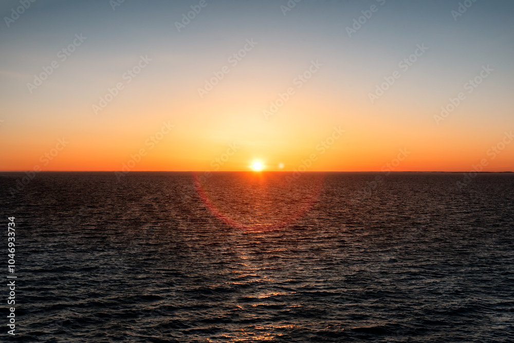 Fototapeta premium Baltic sea at sunset. Clear sky with glowing golden sun, reflections in the water. Setting sun. Epic seascape. Abstract natural pattern, texture, background, concept image