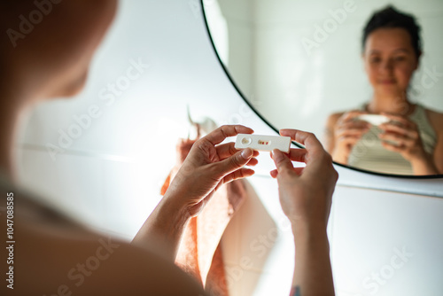 Shocked woman holding positive pregnancy test in bathroom photo