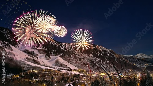 Fireworks explode over a small town nestled in a snowy valley, illuminating the night sky with vibrant colors
