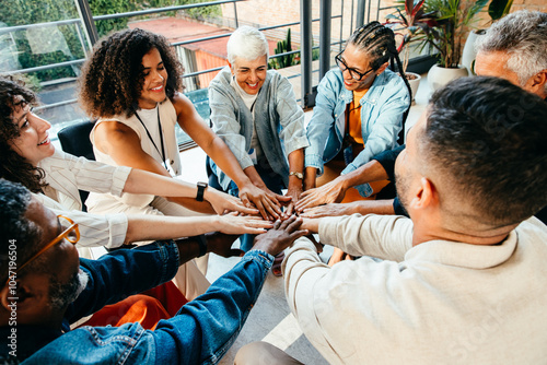 Diverse group of people coming together, placing hands in unity during a team building session in a modern office setting. photo