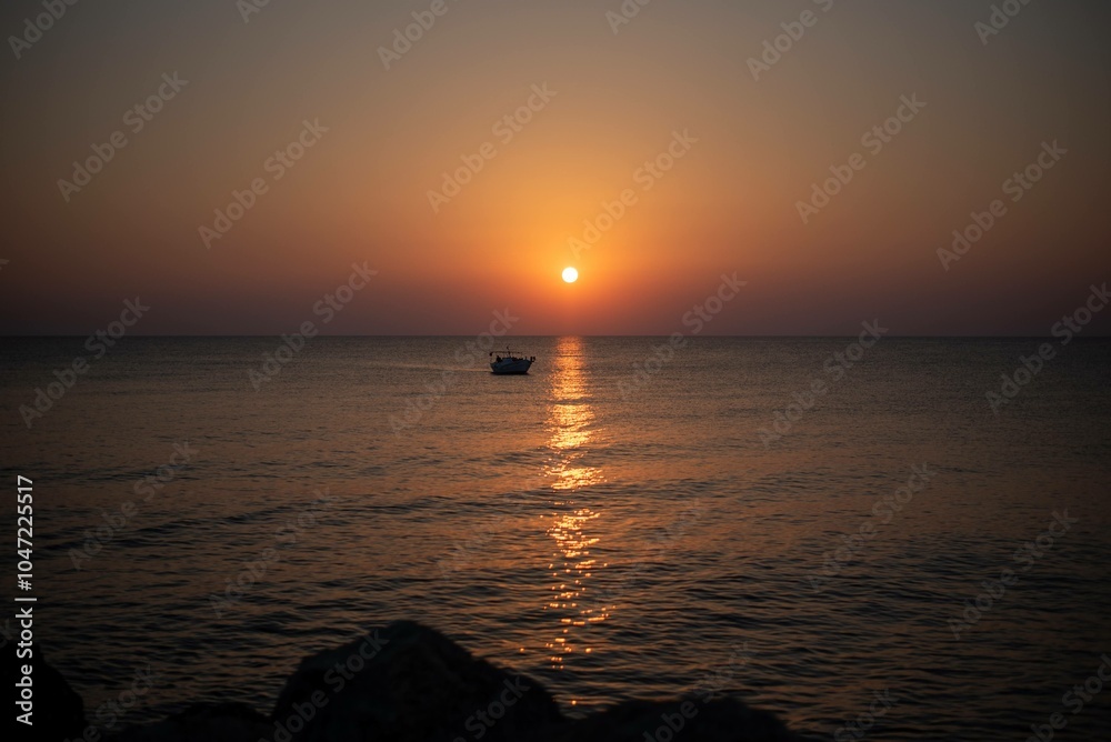 Obraz premium A stunning sunrise over the sea on the island of Crete, Greece. The calm waters reflect the golden hues of the morning sky, creating a peaceful seascape.