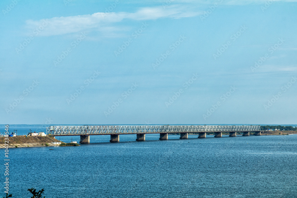 Railway bridge crossing wide river under blue sky with few clouds Railway bridge crossing wide river under blue sky with few clouds