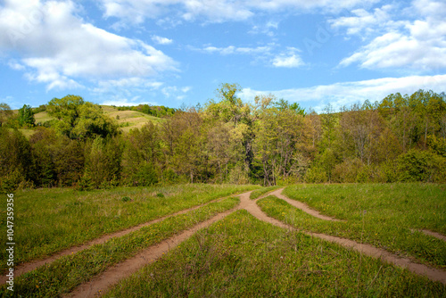 Landscape panorama of green forest and dirt road. The route is paved. Blue clouds in the sky. highway through the forest. Natural landscape.Postcard.For travel and nature trips.