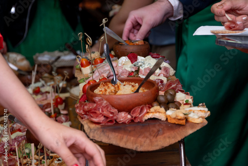 Tabla con fiambres y alimentos salados, primer plano con manos desenfocadas listas para agarrar alimento