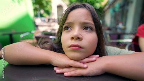 Close-up of a young girl resting her chin on her hands, gazing thoughtfully into the distance. Her expression conveys a sense of contemplation and introspection in an outdoor setting