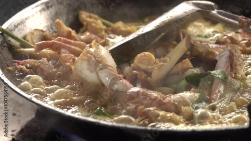 A pan of food is being cooked on a stove. The food is a mix of vegetables and meat, and it is a stir fry. The pan is filled with a variety of ingredients, including shrimp, carrots, and broccoli