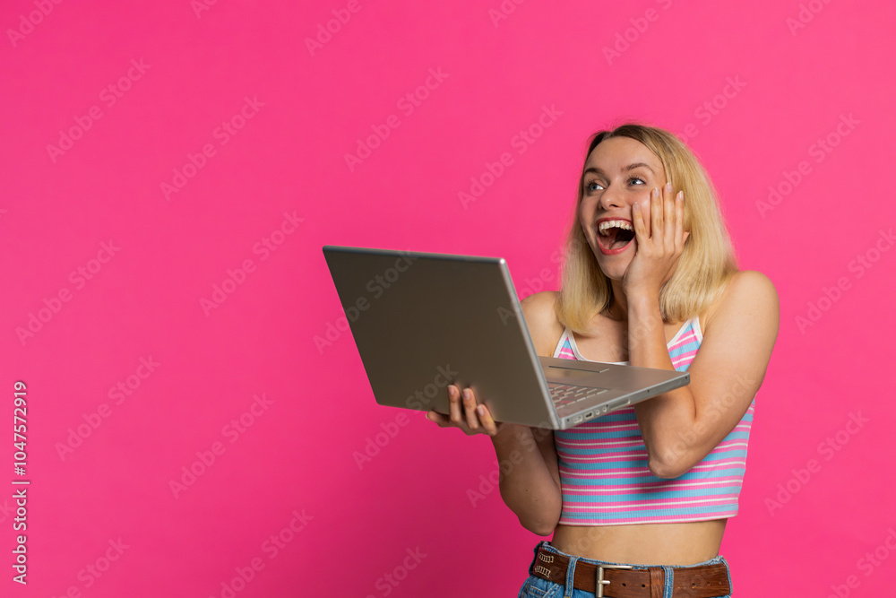 Fototapeta premium Happy excited Caucasian woman typing on laptop, working on project, enjoying results, winning lottery game celebrating success, online shopping victory good email news. Pretty girl on pink background