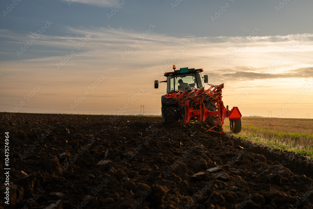 Obraz premium Tractor on the field during sunset.