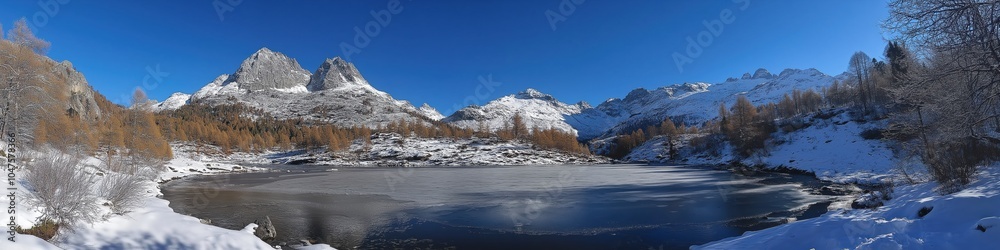 Fototapeta premium A beautiful snowy landscape with a large lake in the middle. The sky is clear and blue, and the mountains in the background are covered in snow. The scene is peaceful and serene