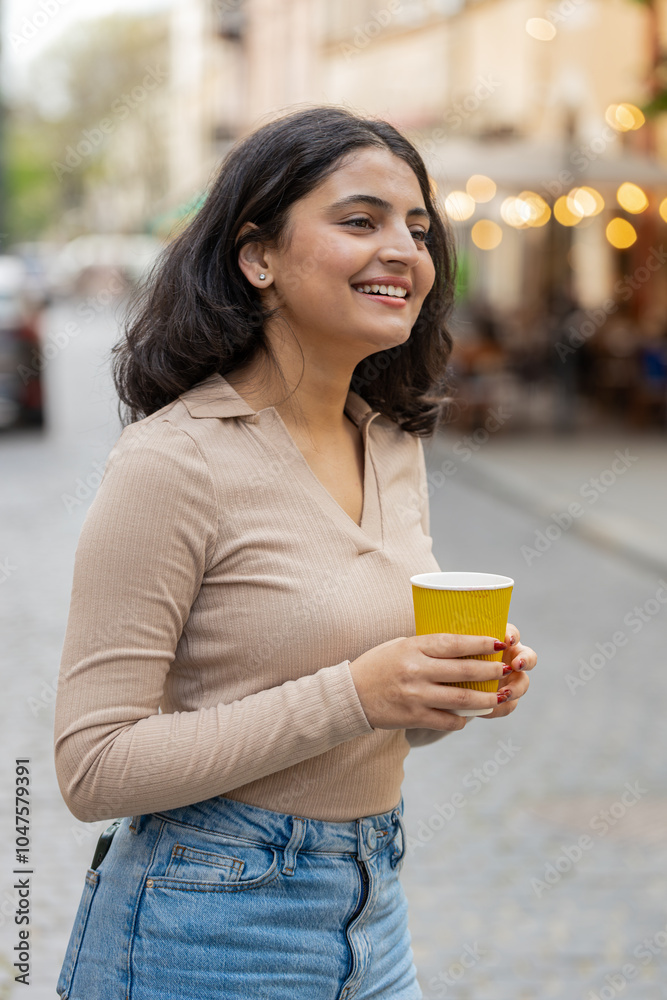Smiling happy Indian young woman enjoying morning coffee hot drink outdoors. Relaxing taking a break. Girl drinking coffee to go walking passes the urban city street. Town lifestyles outside. Vertical Smiling happy Indian young woman enjoying morning coffee hot drink outdoors. Relaxing taking a break. Girl drinking coffee to go walking passes the urban city street. Town lifestyles outside. Vertical