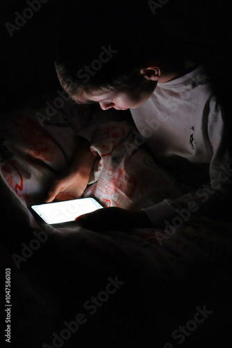 Kid sitting in bed at night with his smartphone on