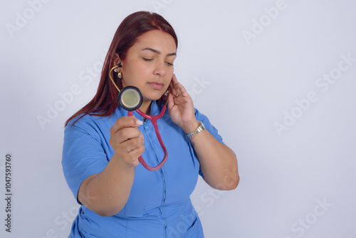 Concentrated Colombian female doctor listening with stethoscope, studio photo, white background