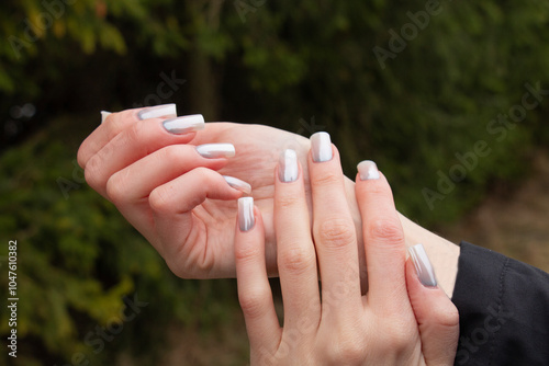 Stylish fashionable manicure of hands woman, pearlescent manicure with a pattern on the background of a Christmas tree branch