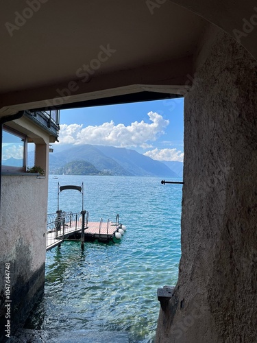 Hidden view of a tranquil lake with clear blue waters, clouds, and mountains in the background. A small dock adds to the serene atmosphere.