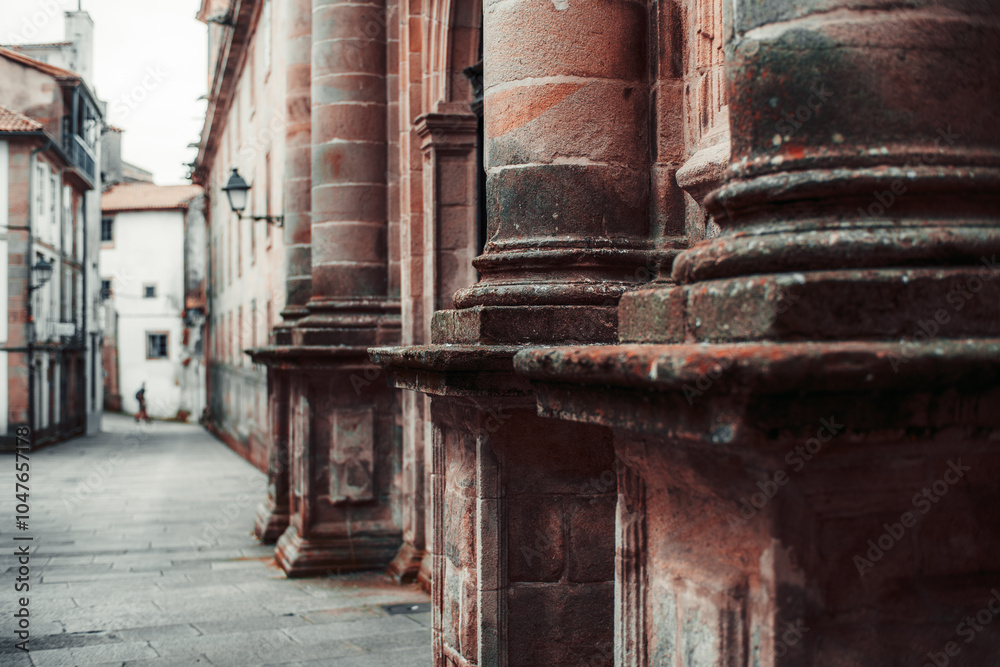Close-up view of weathered stone columns on a historic building facade, showcasing detailed texture and architectural elements. A quiet narrow street fades into the background Close-up view of weathered stone columns on a historic building facade, showcasing detailed texture and architectural elements. A quiet narrow street fades into the background