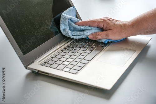 Hand cleaning a dusty laptop with a blue cloth, hygiene at the workplace maintains health, especially with frequently used devices, copy space, selected focus photo