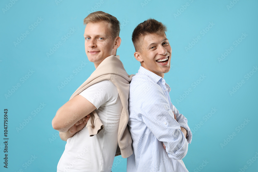 Happy brothers posing with crossed arms on light blue background Happy brothers posing with crossed arms on light blue background