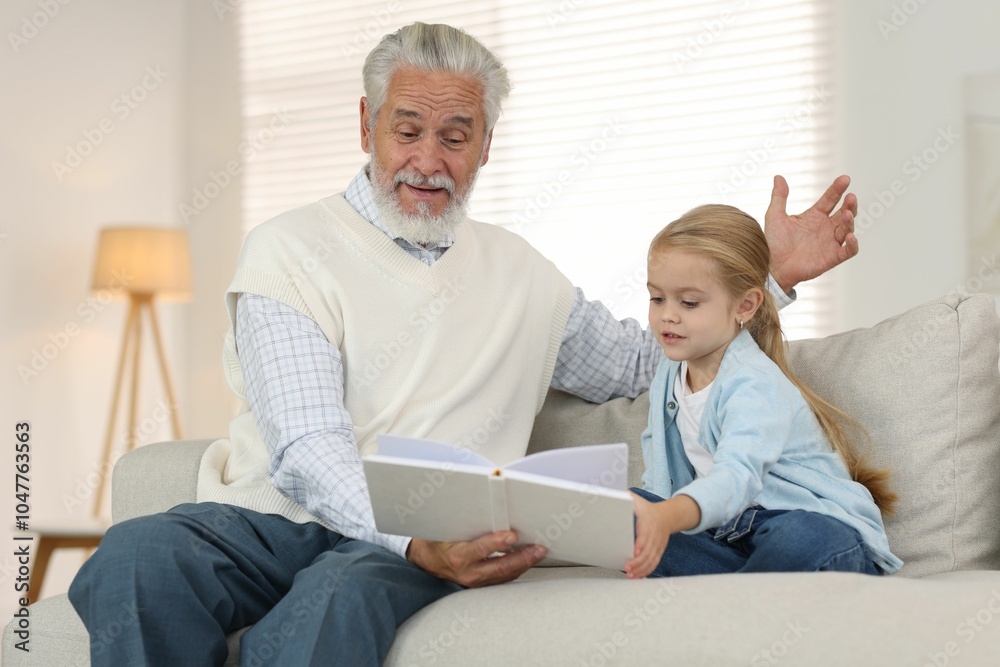 Grandpa and his granddaughter reading book together on sofa at home Grandpa and his granddaughter reading book together on sofa at home