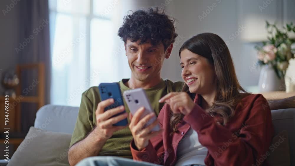 Cheerful couple relaxing sofa looking mobile phones closeup. Spouses talking Cheerful couple relaxing sofa looking mobile phones closeup. Spouses talking