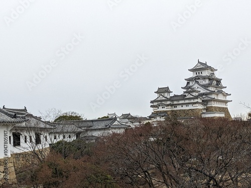 Himeji, Japan - 12.19.2023: Main Keep and the surrounding yagura, or turrets, in Himeji Castle with autumn trees in the garden under a cloudy sky