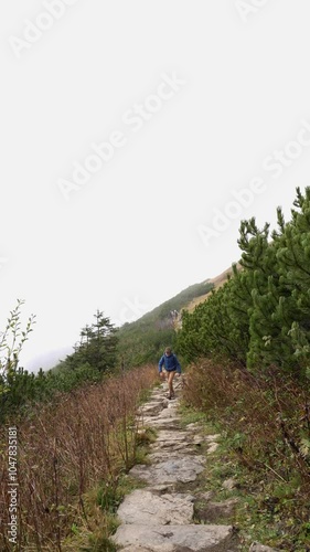 Solitary hiker ascending rugged mountain trail on foggy morning. Concept of adventure, determination, connecting with nature through mountain exploration in misty conditions. High quality 4k footage