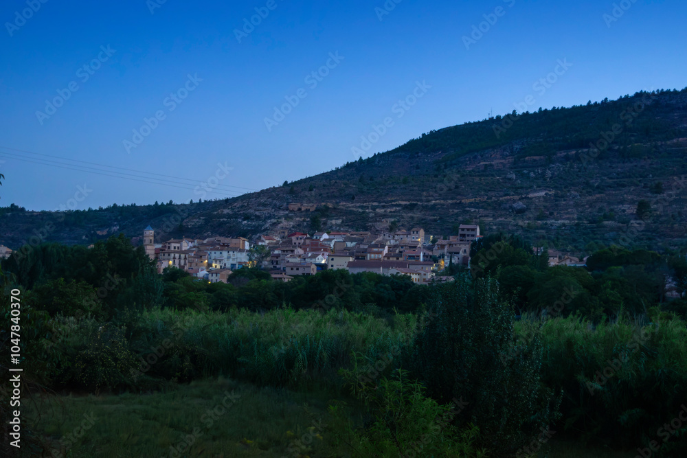 Dusk view of a small village on the Iberian Peninsula, seen from a distance in the countryside, with soft street lights beginning to glow. Casas Altas in Rincón de Ademuz, summer 2023 Dusk view of a small village on the Iberian Peninsula, seen from a distance in the countryside, with soft street lights beginning to glow. Casas Altas in Rincón de Ademuz, summer 2023