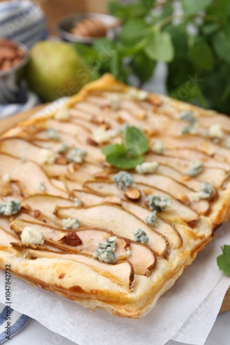 Delicious puff pastry tart with pears, almond, mint and blue cheese on white table, closeup