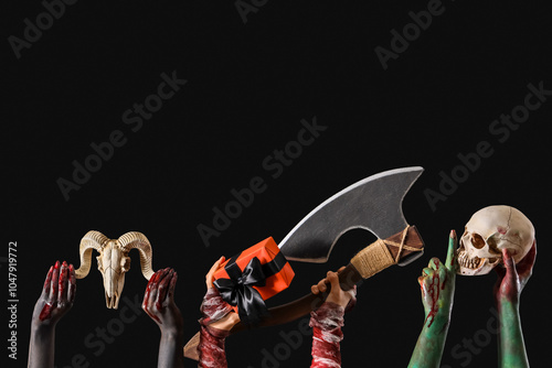 Painted female hands with Halloween gift, axe, human and animal skulls on black background