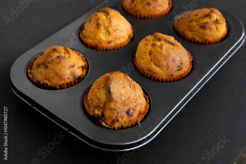Freshly Baked Muffins in a muffin baking pan on dark background. Breakfast or dessert cupcakes viewed from a high angle in muffin tin
