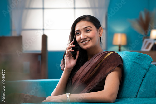 Lovely Housewife Talking On Cell Phone Sitting On Sofa In The Living Room
