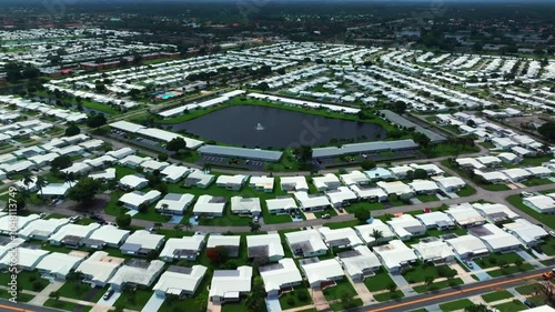 An aerial view of a large 55 and over community in Florida on a cloudy day. The camera tilted downward, dolly in over the property towards a pond with a water fountain in the center. photo