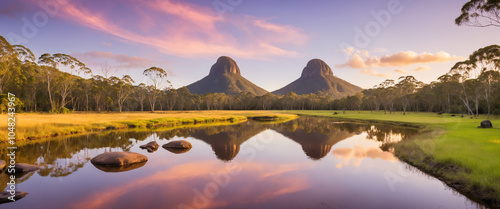 Picture a serene landscape of the Glass House Mountains in Queensland, Australia, with the majestic peaks of Mt. Tibrogargan, Mt. Coonowrin, and Mt. Ngungun rising dramatically from the rolling hills. photo