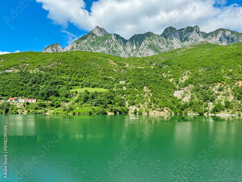 Scenic ferry boat tour on Lake Koman reservoir on Drin river surrounded by forested steep hills, cliffs and mountains of Albanian Alps reflecting in water. Panoramic view along Albanian Fjords. Awe photo