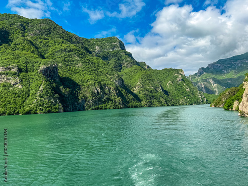 Scenic ferry boat tour on Lake Koman reservoir on Drin river surrounded by forested steep hills, cliffs and majestic rugged mountain ranges of Albanian Alps. Panoramic view along Albanian Fjords. Awe photo