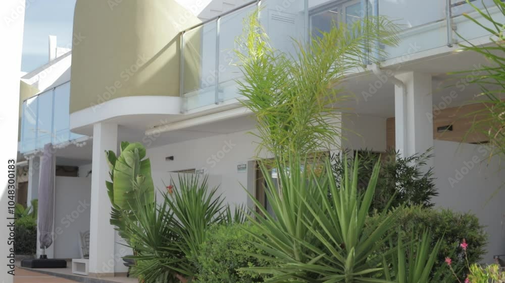 Multiple sequential frames showing gentle breeze blowing leaves of palm trees and other plants in front of modern hotel