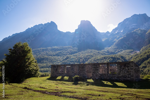 Ruined stone building on alpine meadow with view of majestic mountain massif Zhaborret, Albanian Alps (Accursed Mountains), Valbone Valley National Park, Albania. Scenic hiking trail Valbona to Theth photo